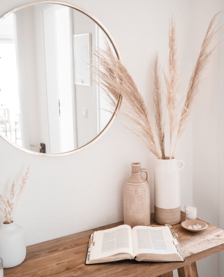 Stimmungsvolles Bild eines Tisches mit Vase, Buch und Spiegel an der Wand